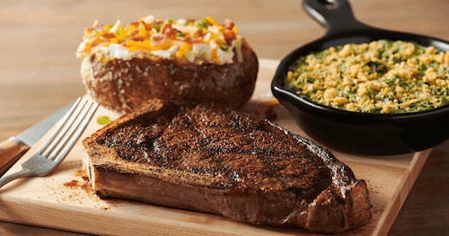 cooked steak on a board with a baked potato and a vegetable casserole in a small cast iron skillet
