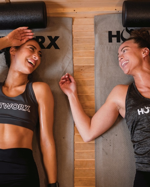 two young women, laughing, laying on their backs on Hotworx yoga mats